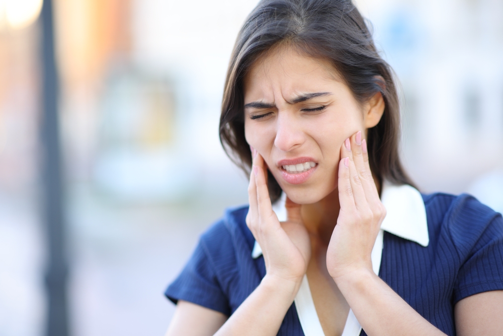 A woman with TMJ pain holding her jaw A woman with TMJ pain holding her jaw
